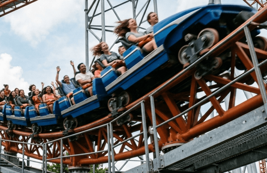 Riders on a rollercoaster train as it banks through a curve, some with their arms in the air.
